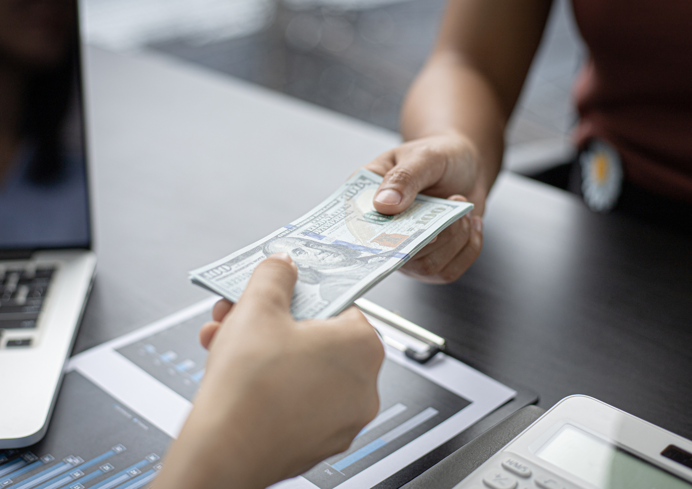 Defensorum Abogados Dos manos intercambiando billetes, simbolizando el blanqueo de capitales.